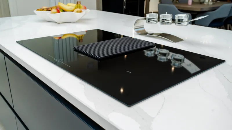 Black venting induction hob set into white quartz kitchen island