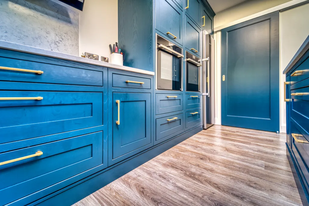 Blue kitchen cabinetry with brass bar handles and integrated double ovens
