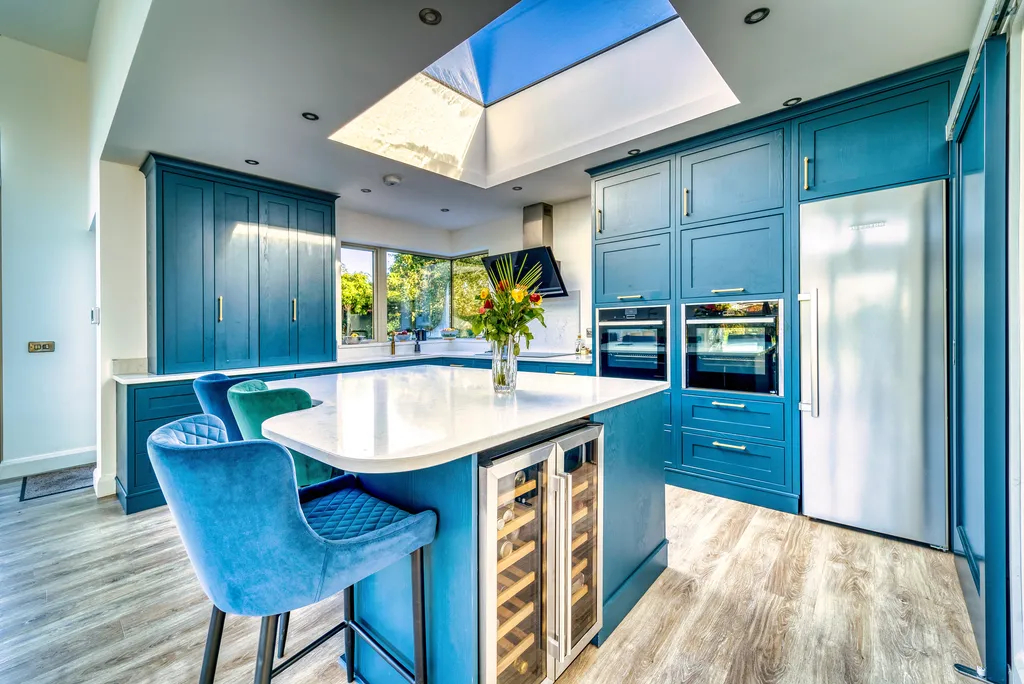 Blue kitchen island with curved quartz worktop, wine coolers and velvet stools