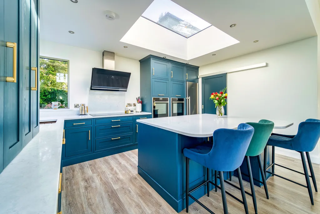 Blue kitchen island with velvet bar stools beneath a large roof lantern
