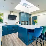 Blue kitchen island with velvet bar stools beneath a large roof lantern