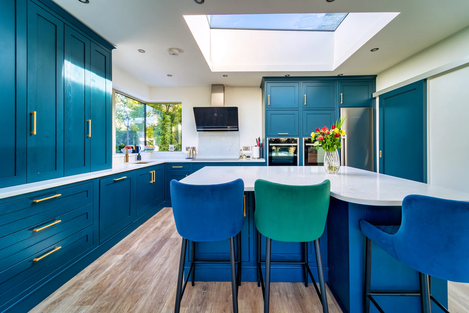 Blue kitchen island with velvet bar stools beneath a skylight