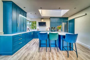 Blue kitchen with tall larder cabinets, island and velvet bar stools