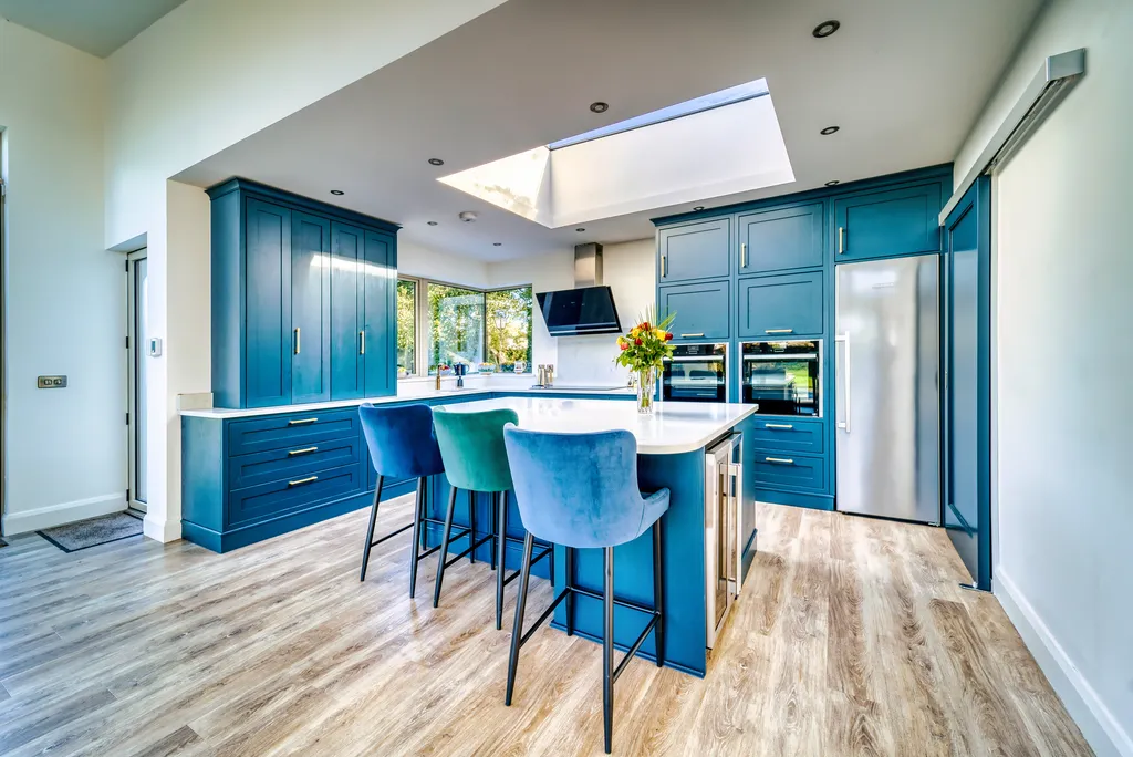 Wide view of blue kitchen with island seating and stainless steel fridge