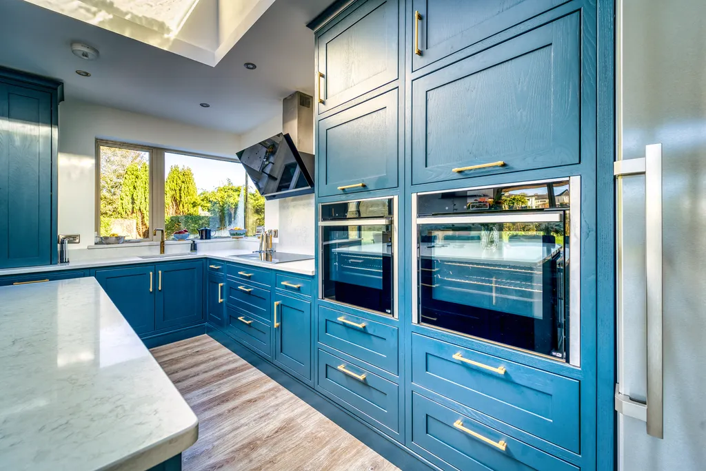 Tall blue cabinets housing double ovens with brass handles and quartz worktops