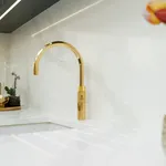Brass swan neck tap on white quartz worktop with marble splashback