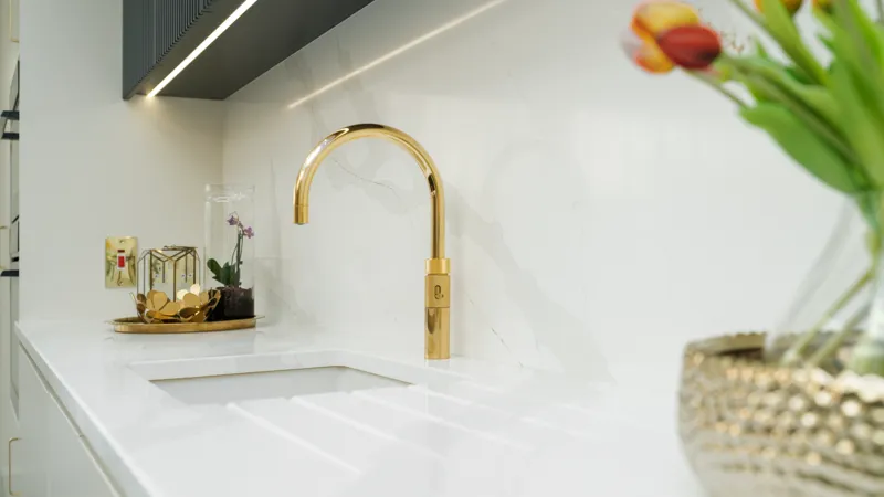 Brass swan neck tap on white quartz worktop with marble splashback
