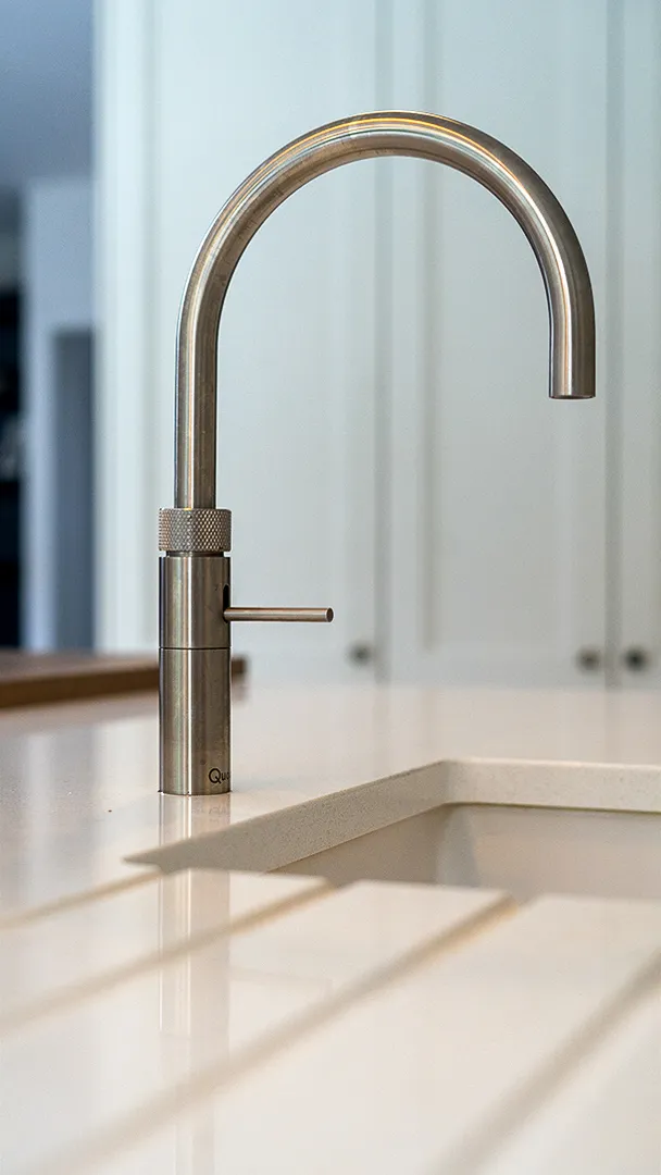 Brushed steel swan neck tap above a white ceramic sink
