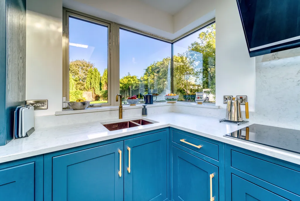 Copper undermount sink with aged brass tap beneath a corner garden window