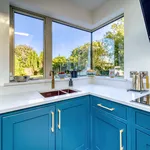 Copper undermount sink with aged brass tap beneath a corner garden window