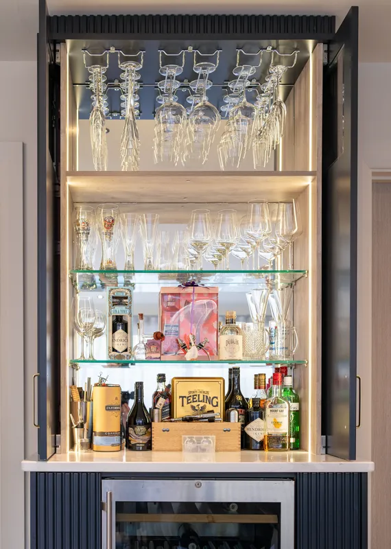 Open home bar cabinet with lit shelving, glassware and spirits
