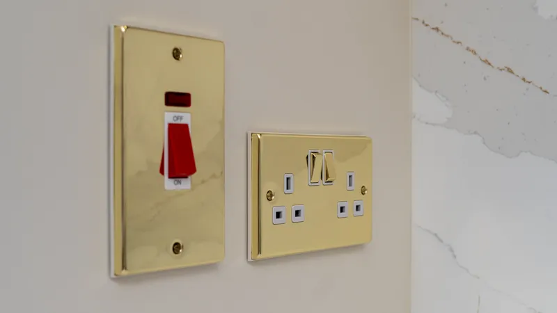 Polished brass cooker switch and double socket on kitchen wall