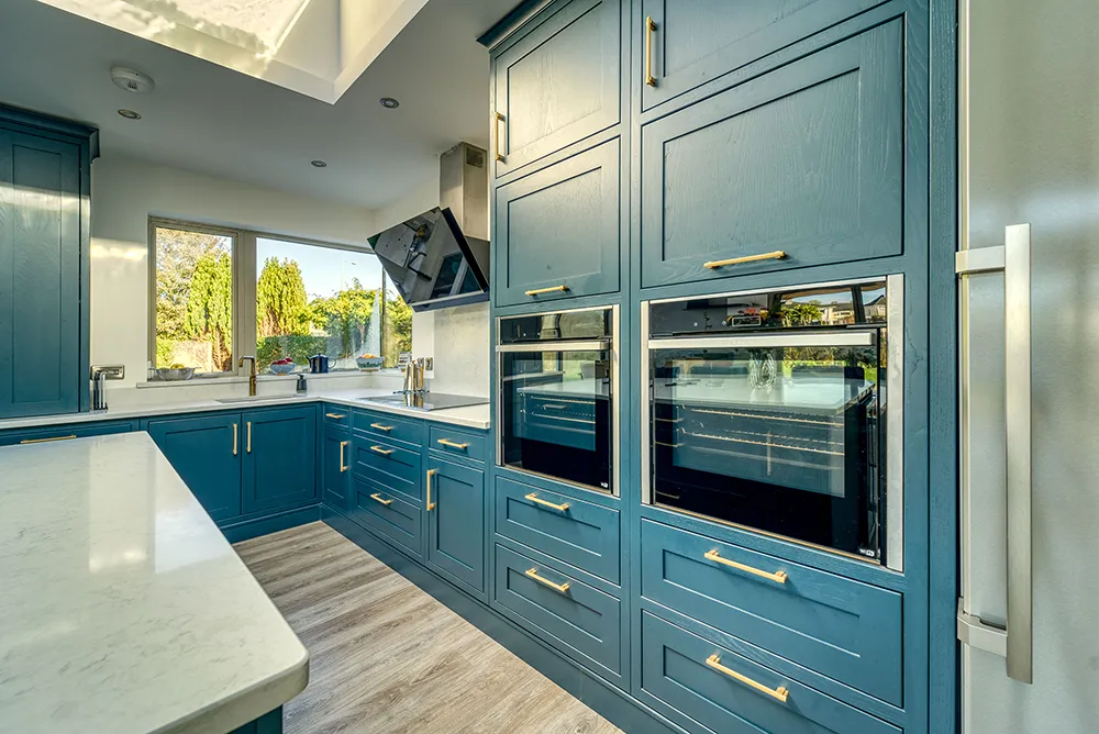 Double built in ovens in teal cabinetry with brass handles