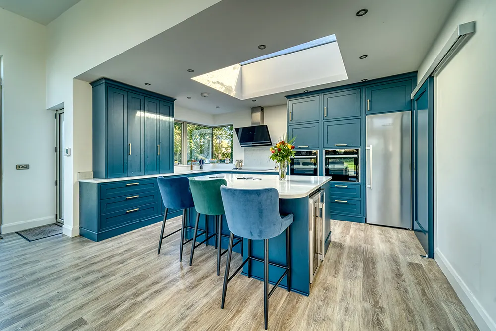 Teal kitchen island with velvet bar stools and wood flooring