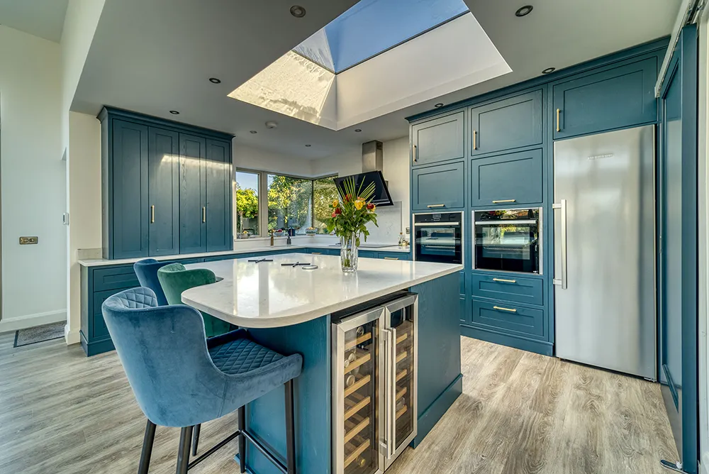 Teal kitchen with tall larders, stainless fridge and island wine cooler