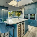 Teal kitchen island with wine fridge and velvet stools beneath a roof lantern