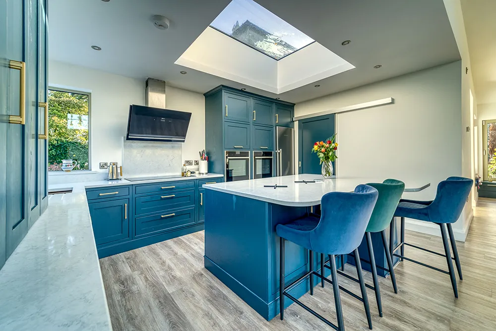Teal shaker kitchen with island seating beneath a large skylight