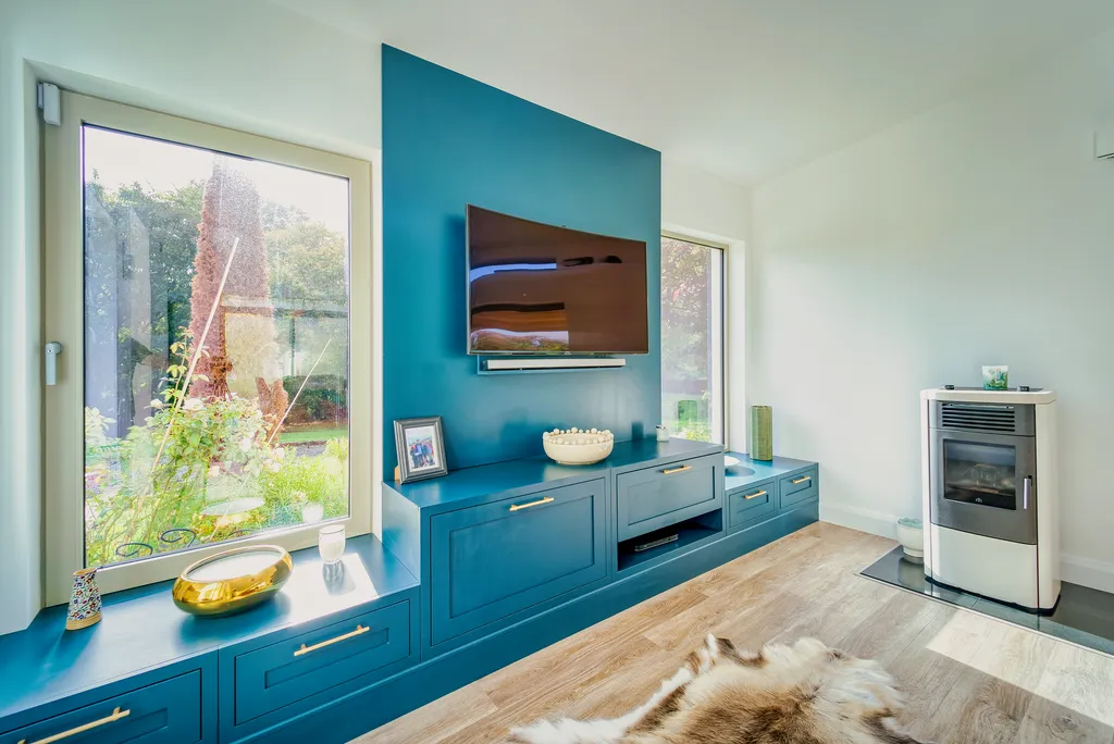 Teal media wall with mounted television, storage cabinets and window seat