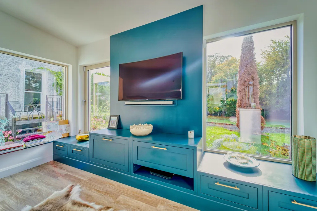 Teal television unit flanked by windows with garden views