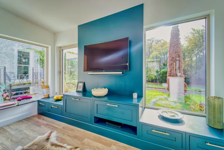 Teal television unit flanked by windows with garden views