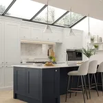 White shaker kitchen with navy island and bar stools beneath a glazed roof