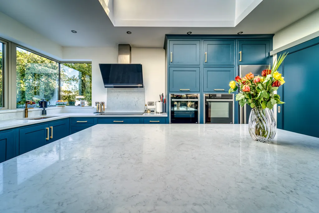 White quartz island worktop facing blue tall units and integrated ovens